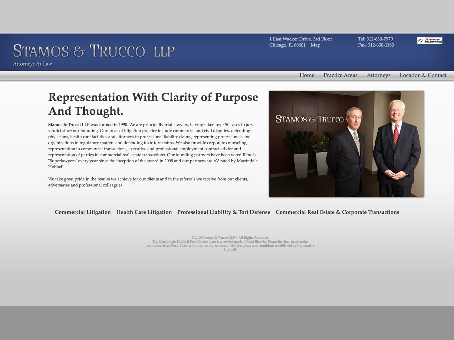 A screenshot of a website showing a subtle blue navigation bar with the title Stamos & Trucco LLP in a stately font and shiny, silver appearance on the left and address information to the right. Some links in blue are seen in the bar and below that in the main section is illegible copy save for the page heading "Representation with clarity of purpose and thought" and to the right a photo of two men with grey hair and dark blue and grey, tailored suits standing in front of a desk